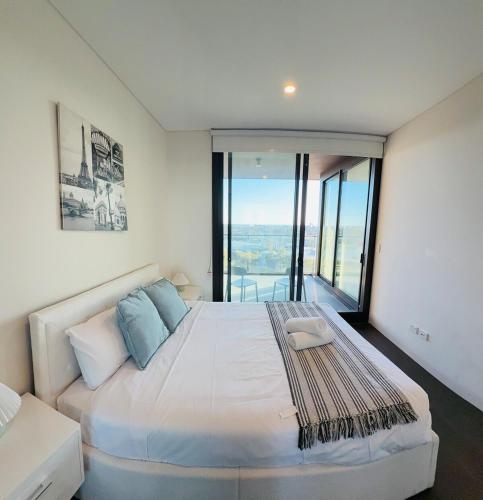 a bedroom with a large white bed with a view at Olympic Park Stylish Apt with Gym Pool great view in Sydney