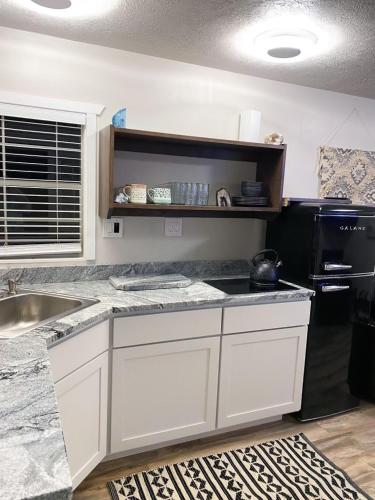 a kitchen with white cabinets and a black refrigerator at Glitter and Grit! The Wild West 40 Homestead in Cane Beds