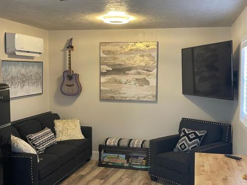 a living room with two black couches and a guitar at Glitter and Grit! The Wild West 40 Homestead in Cane Beds