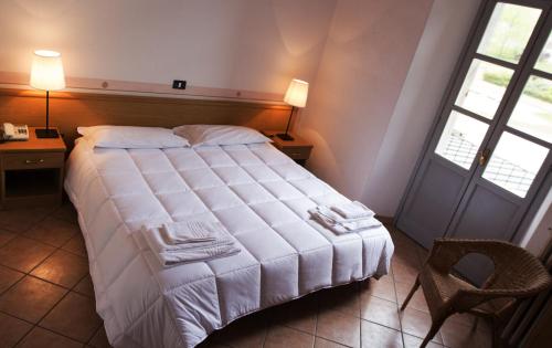 a bedroom with a bed and a chair and two windows at Hotel Portici in Vicoforte