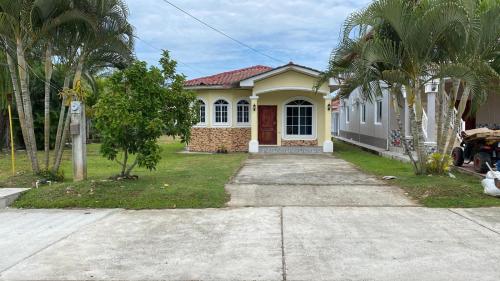 a small yellow house with palm trees and a driveway at Residencial Costa Mar in Puerto Cortes