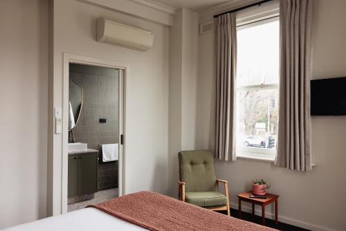 a bedroom with a bed and a chair and a bathroom at Naughtons Hotel in Melbourne