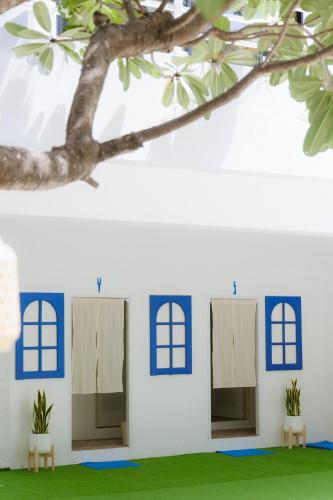 a white wall with blue windows and a tree at Sheva Om in Ban Wat Pho Thong