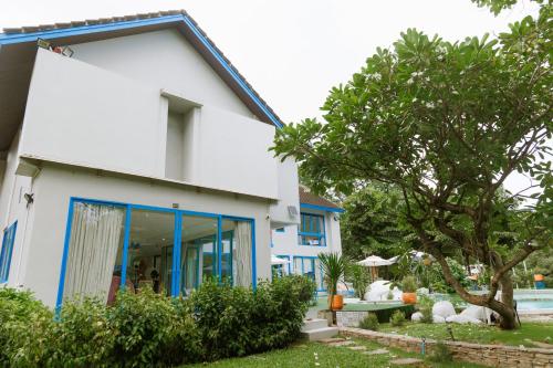 a white house with blue windows and a tree at Sheva Om in Ban Wat Pho Thong