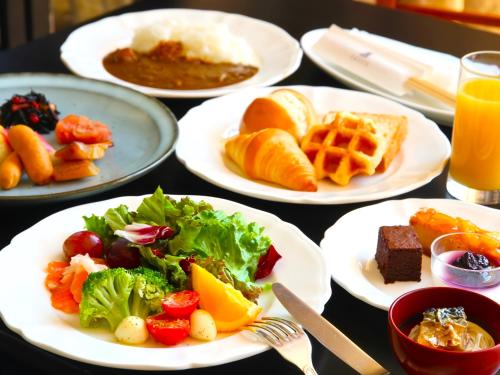 a table with plates of breakfast foods and orange juice at Kitabiwako Hotel Grazie in Nagahama