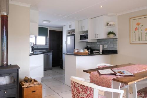 a kitchen and dining room with white cabinets and a table at High Season Farm Luxury Cottages in Hermanus