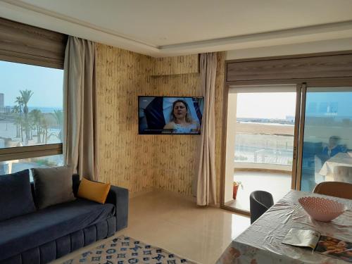 een woonkamer met een bank en een tv aan de muur bij Appartement vue sur mer, terrasse ensoleillée in Asilah