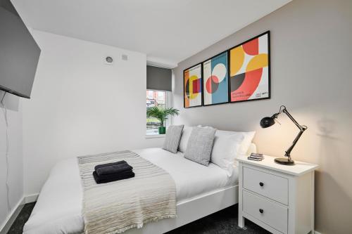 a white bedroom with a bed and a lamp on a night stand at Luxury Lower-Level Two Bed Apt in Headingley