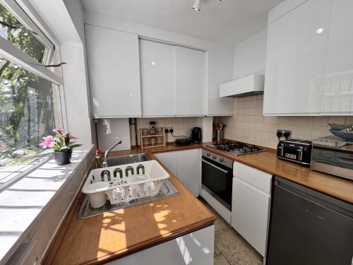 a kitchen with white cabinets and a sink at Stylish Entire Apartment with Private Garden in Camden, Central London in London