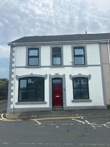 a white house with a red door on a street at The Greenfield Inn Guest House in Llanelli