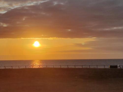 a sunset on the beach with the ocean and a fence at 2 Bedroom Guest House Near Beach in Llanelli