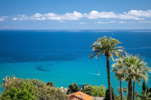 a view of the ocean with palm trees and a house at LE NEPTUNE - Vue Mer - Grande terrasse - Parking Privé in Menton