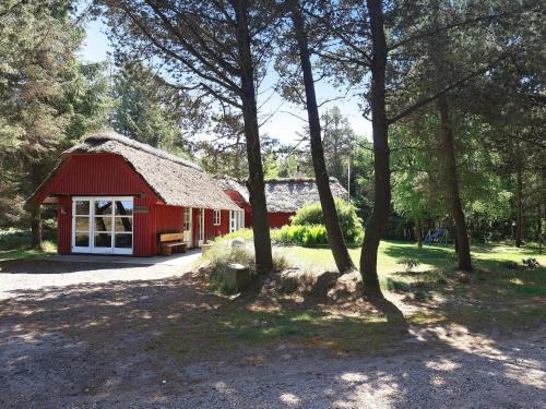 a red barn with a grass roof in a forest at 4 star holiday home in Blåvand in Blåvand