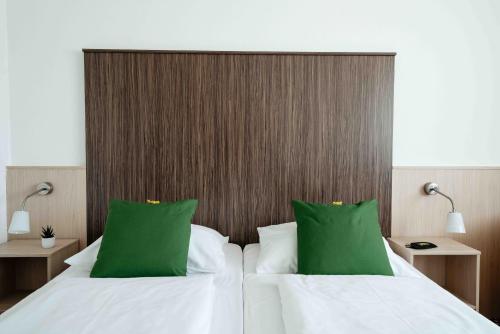 a bedroom with two white beds with green pillows at SLEEEP Hotel Vösendorf in Vösendorf