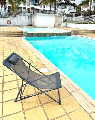 a chair sitting next to a swimming pool at Ti DODO Studio Cosy accès piscine in Saint-Pierre