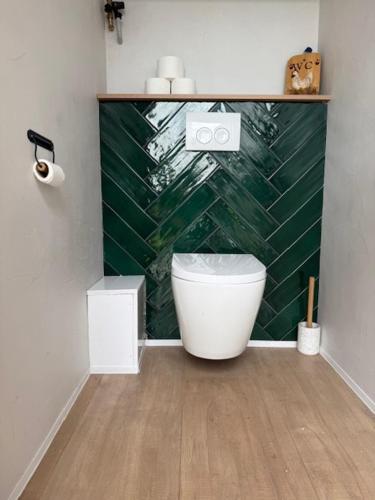 a bathroom with a toilet and a green tiled wall at 't Hoevehuisje in Beverwijk