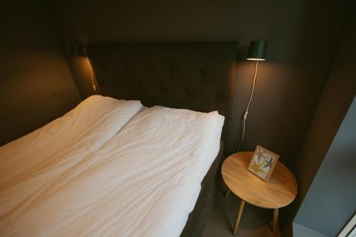 a bed with a white sheets and a table with a lamp at #Lofoten Leilighet ved sjøen in Ballstad