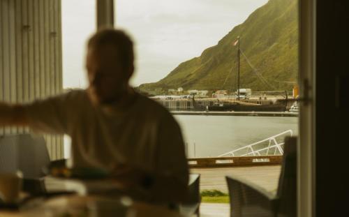 a man is looking out a window at a marina at #Lofoten Leilighet ved sjøen in Ballstad