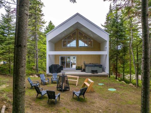 a house in the woods with chairs and a grill at Spa Babyfoot Total comfort - Le Chouette Chalet in Saint-Donat-de-Montcalm