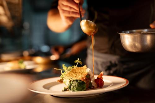 a person is pouring sauce on a plate of food at Hotel Maximilian in Bad Griesbach