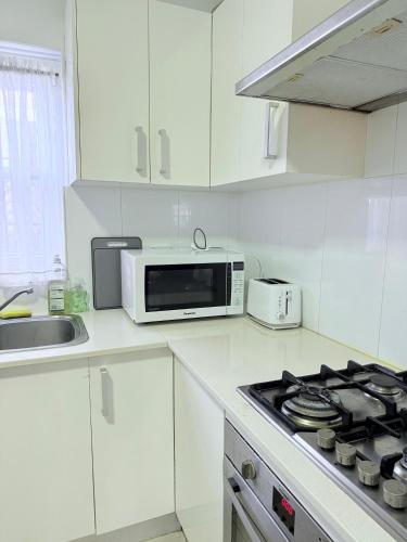 a white kitchen with a microwave and a stove at Shipradi Homes - Prime location near shops & eatery in Sydney