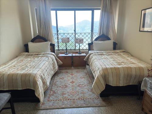 two beds in a room with a window at Starry Nights by Demanchi in Bhurban