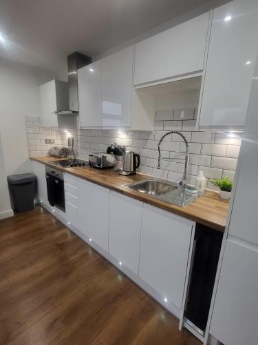 a kitchen with white cabinets and a sink and wooden floors at Forest Gate Nest Nottingham in Nottingham