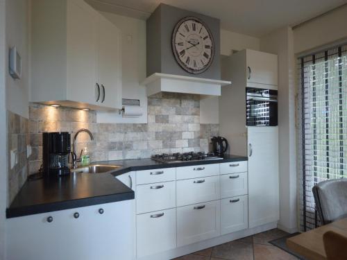 a kitchen with white cabinets and a clock on the wall at Holiday Home near Sallandse Heuvelrug in Lemele