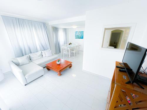 a white living room with a white couch and a tv at LOS CORALES Resort VILLAS & Apartments WIFI BEACH Club & SPA in Punta Cana