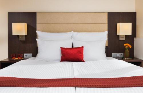 a bedroom with a large white bed with a red pillow at Leonardo Hotel Munich Arabellapark in Munich