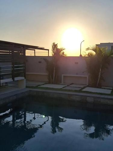 a swimming pool with the sun setting behind a building at Harmonious Villa in Flic-en-Flac with Private Pool in Flic-en-Flac