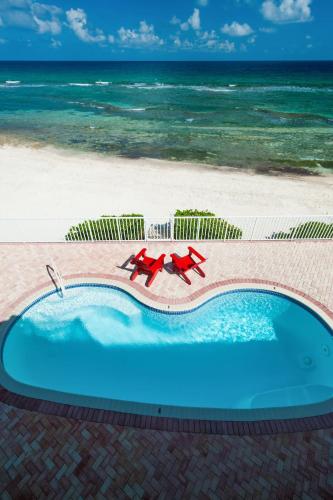 a swimming pool with two red chairs and the beach at Parrot-ise 4 Bedroom Villa in Brinkleys