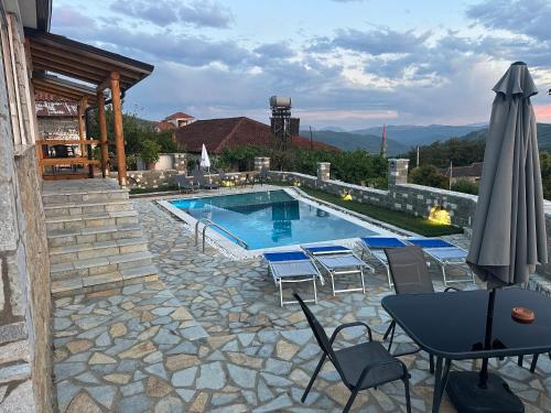 a swimming pool with a table and chairs and an umbrella at Mimani Stone House Roshnik in Roshnik