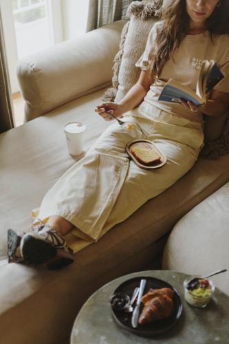 a woman sitting on a couch with a book and a plate of food at Village Aparthotel By BOA in Porto