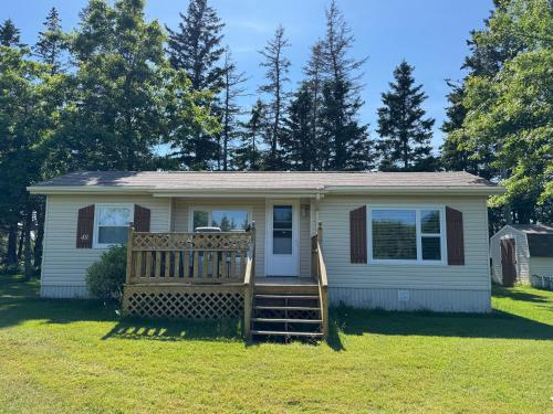 a small white house with a porch and a yard at Hidden Acres Cottages in Cavendish