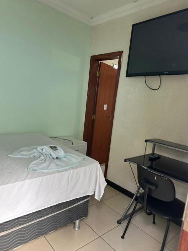 a room with a bed and a desk and a flat screen tv at Hotel Industrial Contagem in Contagem