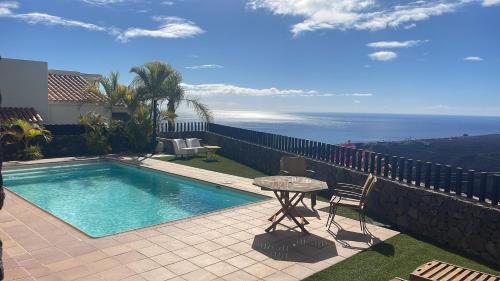 a swimming pool with a table and chairs and the ocean at Villa La Pintora in Playa de Santiago