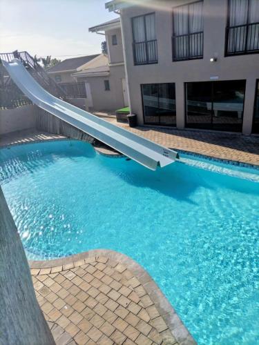 a swimming pool with a slide in front of a house at Banana Beach Getaway in Port Shepstone