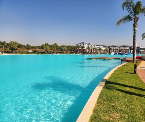 a large swimming pool with blue water and palm trees at 1 Bed Crystal Lagoon Escape in Pretoria