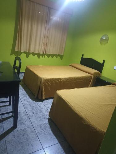 two beds in a room with green walls and a table at Hostal Villa María in La Nava de Ricomalillo