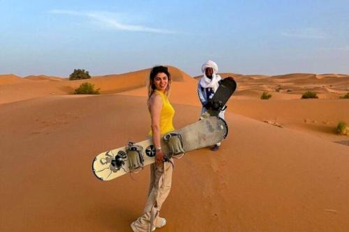 a woman holding a snowboard in the desert at Merzouga Desert Tents in Merzouga