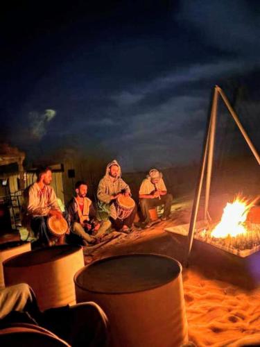 a group of people sitting next to a fire at Merzouga Desert Tents in Merzouga