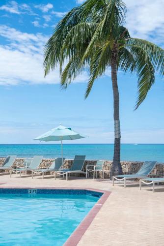 a palm tree and a swimming pool next to the ocean at Plantation Village #37 Condo in Seven Mile Beach