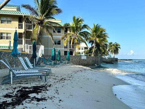 a beach with chairs and umbrellas and the ocean at Plantation Village #37 Condo in Seven Mile Beach
