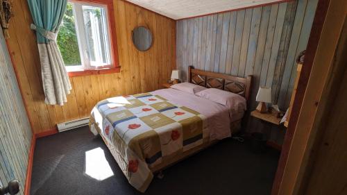 a bedroom with a bed in a room with a window at Grangette Entre Chiens et Loups in LʼAnse-Saint-Jean