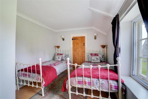 two beds in a white room with a window at Cockleshells in Castle Acre