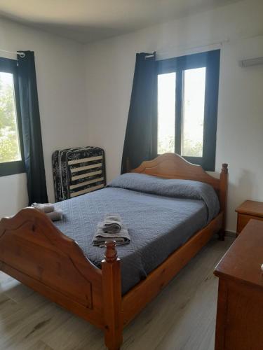 a bedroom with a wooden bed with blue sheets and two windows at Pomos rockaway beach house in Pomos