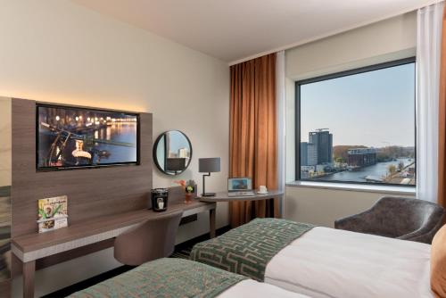 a hotel room with a bed and a desk and a window at Leonardo Royal Hotel Amsterdam in Amsterdam