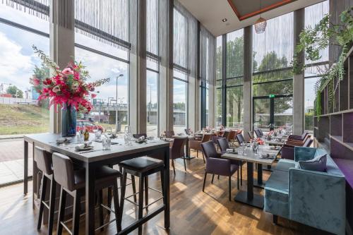 a dining room with tables and chairs and windows at Leonardo Royal Hotel Amsterdam in Amsterdam
