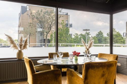 a dining room with a table and chairs and large windows at Leonardo Hotel Lelystad City Center in Lelystad